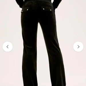 Svarta velourbyxor Juicy Couture M - Svarta mjukisbyxor från Juicy Couture i mjuk velour. Byxorna har raka ben, bred resår i midjan och två bakfickor med lock och silvriga knappar med JC-logga. Perfekta för en chill och trendig look.