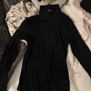 Svart polotröja från H&M - En svart, ribbad polotröja från H&M Basics i storlek S. Tröjan har lång ärm och hög krage, perfekt att styla lager på lager eller bära som den är. Enkel och stilren design som funkar till många olika looks.