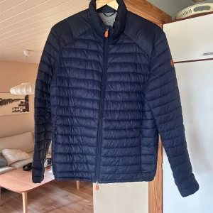 Mörkblå pufferjacka Save The Duck - Säljer en mörkblå pufferjacka från Save The Duck i storlek L. Jackan är ultralätt med vattenavvisande och ventilerande Plumtech-material, har ståkrage och hel dragkedja framtill. Snygg quiltad design och diskret logga på ärmen. Perfekt för kyliga dagar.