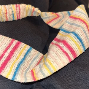 Randigt diadem från Djerf Avenue - Säljer ett färgglatt diadem från Djerf Avenue med smala ränder i rosa, blått, gult och vitt. Tillverkat i en mjuk mix av återvunnen bomull och polyester. Perfekt accessoar för att liva upp din look med en lekfull touch.