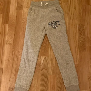 Grå mjukisbyxor från GANT  - Snygga grå mjukisbyxor från GANT med vit dragsko i midjan och tryckt logga på ena benet. Byxorna har ribbade muddar vid benslut och två fickor fram. 