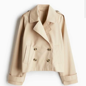 Beige trench coat  - Snygg beige kappa med dubbelknäppning och klassisk krage. Jackan har en croppad design och axelklaffar för en stilren look. 