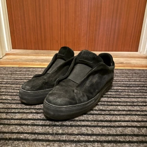 Axel Arigato 360 - Säljer ett par helsvarta sneakers från Axel Arigato i mjuk mocka. Skorna har minimalistisk design utan snörning, med diskret logga i guld på sidan och tjock svart sula. Perfekta för dig som gillar stilrena och cleana skor med en modern vibe. Skorna har använts med kärlek som ni ser & det ger skorna lite karaktär. Den enda tydliga defekten är att sömmen har öppnats väldigt lite som ni ser på sista bilden. Skorna är i 43 och passar både 43 & 44