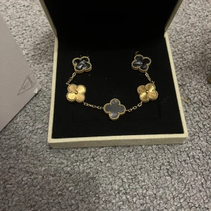 VAN CLEFF armband - Exklusivt Alhambra armband  med ikoniska fyrklöver i blått och svart. Armbandet har en tunn guldfärgad kedja och levereras med originalask, påse och äkthetsintyg. Perfekt för dig som älskar lyxiga detaljer och tidlös design.