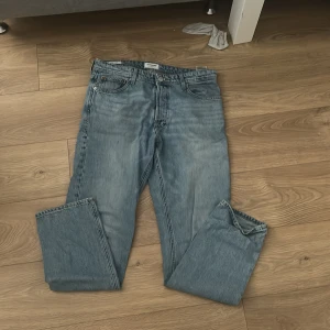 Jack & Jones Loose Chris ljusblå jeans - Ljusblå jeans från Jack & Jones i modellen Loose Chris. Jeansen har en loose fit med raka ben, klassisk femficksdesign och knappgylf. Tillverkade i bomull med snygg tvättad look och kontrastsömmar. Perfekta för en avslappnad stil.