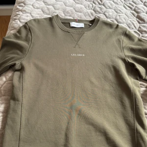 Olivgrön sweatshirt från Les Deux - Snygg olivgrön sweatshirt från Les Deux med diskret logotyp broderad på bröstet. Tröjan har rund hals, ribbade muddar och klassisk passform. Använd väldigt lite. Kan gå ner i pris. Säljer av garderoben 