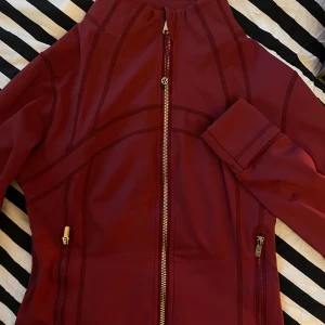  Lululemon jacka burgundy - GÅR NER I PRIS OM DEN KÖPS INNAN 6e NOVEMBER!! Snygg vinröd träningsjacka från Lululemon med guldiga dragkedjor och detaljer. Jackan har figurnära passform, lång ärm och två fickor med dragkedja. Materialet är mjukt och stretchigt syntet, perfekt för aktiva dagar.