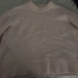 Ljusrosa stickad tröja med ribbade detaljer - Mysig ljusrosa stickad tröja med rund halsringning och breda ribbade muddar vid ärmslut och nederkant. Perfekt för lager-på-lager och chill dagar. Enkel och stilren design som passar till det mesta.