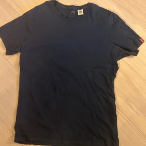 Mörkblå t-shirt från Levi's i bomull - Säljer en stilren mörkblå t-shirt från Levi's i mjuk bomull. Klassisk rund hals och korta ärmar, med den ikoniska röda Levi's-taggen på ärmen. Perfekt för dig som gillar enkel och clean look.