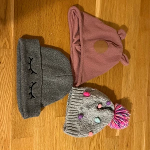 Tre mössor: McKinley, Angels, grå med brodyr - Säljer tre mössor! En rosa fleece-mössa från McKinley med söta öron och rund patch, en grå stickad mössa med broderade ögonfransar, samt en grå stickad Angels-mössa med färgglada bollar och stor rosa/vit/lila tofs. Perfekt för dig som gillar gulliga detaljer och färg.