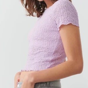 Ljuslila topp Gina Tricot - Supersöt ljuslila topp från Gina Tricot i storlek XS. Den har korta ärmar, ribbad och krusig struktur samt en lätt vågig kant vid halsen och lite genomskinlig.