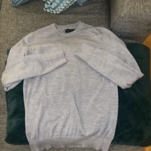 Ljusgrå merinoullströja från Riley - Säljer en stilren ljusgrå tröja från Riley i mjuk merinoull. Tröjan har rund halsringning, långa ärmar och en klassisk passform. Perfekt för lager-på-lager och enkel att matcha med jeans eller chinos.