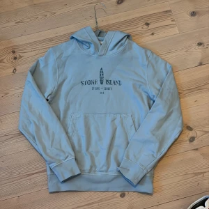 Ljusblå hoodie från Stone Island - Pris kan diskuteras! Den passar ungefär 150 164 då den är stretchig. Snygg ljusblå hoodie från Stone Island med tryck både fram och bak. Klassisk känguruficka och huva, perfekt för dig som gillar streetwear. Mjuk bomullskvalitet och relaxed fit. Stort logotryck på ryggen och mindre print på bröstet.