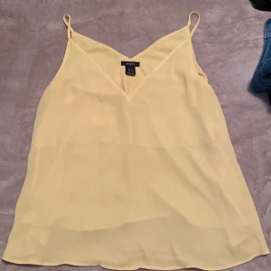 Gul linnetopp från Lindex - Säljer en ljusgul linnetopp från Lindex i storlek M. Toppen har smala axelband och v-ringning framtill, perfekt för varma dagar. Materialet är lätt och luftigt, vilket gör den superbekväm att bära.