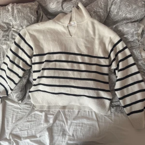 Vit och svart randig stickad tröja Gina Tricot - Säljer en vit stickad tröja från Gina Tricot med svarta horisontella ränder. Tröjan har en krage med v-ringad öppning, ribbade muddar och nederkant. Perfekt för dig som gillar klassisk och chill stil.