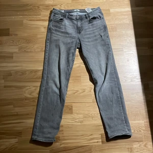 Grå raka jeans från Jack&Jones  - Snygga grå jeans från Nudie med klassisk femficksdesign och raka ben. Jeansen har en tvättad look och subtila sömdetaljer på bakfickorna. Perfekta för en avslappnad stil och lätta att matcha med det mesta.