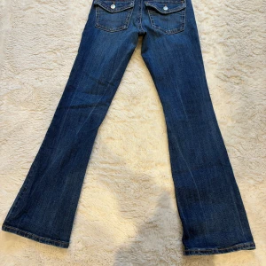 Blå bootcut jeans med slitningar, strl 34 - Snygga blå bootcut jeans från Gina tricot i storlek 34. Jeansen har slitna detaljer och hål på knäna för en cool, avslappnad look. Klassisk femficksmodell med ficklock bak och kontrastsömmar. Perfekta för dig som gillar en trendig och avslappnad stil. Hör av dig om frågor.💕