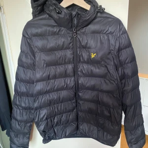 Svart Lyle & Scott pufferjacka - En väl omhändertagen Lyle and Scott pufferjacka. Den har ett pyttelitet hål/snitt på ryggen, men ingenting som märks tydligt. Jackan kostade 900 kronor som nyköpt
