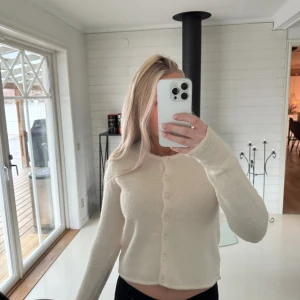 cremevit  kofta från Gina Tricot - Supermjuk och mysig cremevit  kofta från Gina Tricot med rund halsringning och knappar hela vägen framtill. Långärmad och i en stickad, fluffig kvalitet som känns lyxig. Perfekt att slänga på sig när det är lite kyligt ute.