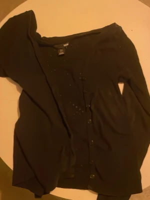 Svart kofta från H&M med knappar - En enkel svart kofta från H&M i storlek S. Koftan har långa ärmar och stängs med svarta knappar framtill. Tillverkad i ett mjukt och tunt material som passar perfekt till lager på lager. Klassisk och lättmatchad modell.