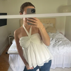 Vit Nelly topp  - Supersöt vit blus med halterneck och knyt i nacken. Toppen har omlott-detalj framtill och är gjord i ett tunt, flowy material som ger en luftig känsla. Perfekt till jeans eller kjol för en fräsch sommarlook. Så snygg storlek S använd två ggr
