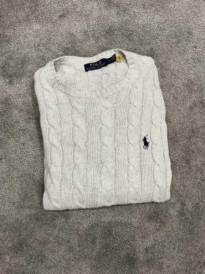 Ljusgrå kabelstickad tröja  Ralph Lauren - Säljer en ljusgrå kabelstickad tröja från Polo Ralph Lauren. Perfekt till lager på lager och riktigt snygg till jeans eller kjol. Säljer den främst för att den inte används så mycket längre. Modellen är 183cm och väger 71 kg. Pris kan diskuteras