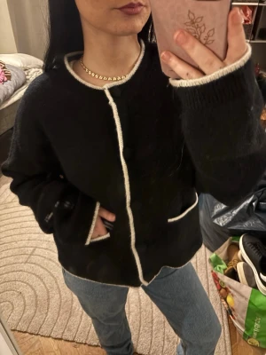 Världens Goaste Alpacka/ull blend Cardigan🩷🖤 - Mysig svart Alpackablend kofta med vita kontrastkanter och rund hals. Koftan har knappar framtill och två fickor med vit kant. Modellen är loose fit och har långärmade ärmar. Materialet är stickat och känns fluffigt och mjukt. Strl L men passar perfekt på mig som är xs/s❤️
