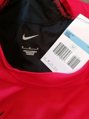 Röd Nike t-shirt med svart detalj - Snygg röd t-shirt från Nike med svart meshpanel upptill och svart Nike-logga på bröstet. Tillverkad i lätt och funktionell polyester, perfekt för träning. Klassisk rund hals och korta ärmar för en sportig look. Stor i storlek, motsvarande Large (L) 