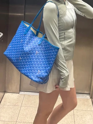 Blå shoppingväska  - Säljer en ikonisk blå shoppingväska med långa handtag. Väskan är rymlig och har beige insida samt detaljer i blått. Perfekt för dig som vill ha en statement bag med plats för allt du behöver. Har en fläck på insidan som jag inte testat ta bort!