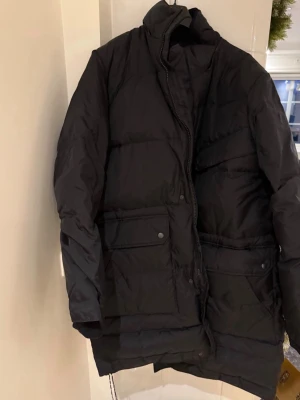 Tiger of Sweden Jacka dunkappa HELT NY  - Tiger of Sweden vinterjacka i storlek L, svart färg och fyllning av dun (inte att förväxla med de billiga polyesterfyllningarna).  Stor i storleken kappa dunjacka lång modell  Finns även tillhörande luva som medföljer