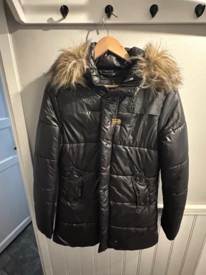 Svart pufferjacka från G-Star RAW - Säljer en svart pufferjacka från G-Star RAW med snygg fuskpäls på huvan. Jackan har dragkedja, knappar, två fickor framtill och ribbade muddar vid ärmsluten. Perfekt för kalla dagar och riktigt skön att bära. Stilsäker och varm jacka för vintern!