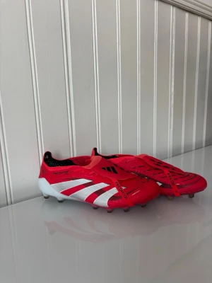 Adidas Predator röda fotbollsskor - Säljer ett par Adidas Predator fotbollsskor i rött med vita och svarta detaljer. Dobbarna är i väldigt bra skick. Säljer dom för att jag köpta för liten storlek och växte ut dom. Sparsamt använda och köpta från unisports.