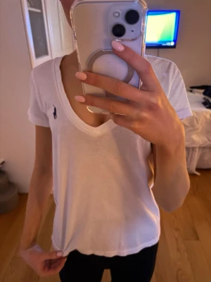 Vit v-ringad t-shirt från Ralph Lauren - Klassisk vit t-shirt från Ralph Lauren med v-ringning och korta ärmar. T-shirten har den ikoniska lilla marinblå loggan broderad på bröstet.   Säljer eftersom att den inte har kommit till användning mycket alls. Storlek XS/S! Köpt för ungefär 700 kr.