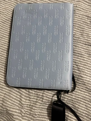 Blå datorväska från Carin Wester - Snygg blå datorväska från Carin Wester med präglad CW-logga över hela framsidan. Väskan har svart axelrem och dragkedja, samt en stilren insida med logopatch. Perfekt för att bära laptop och viktiga grejer till plugget eller jobbet.