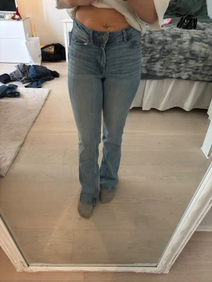 Ljusblå bootcut jeans med hög midja - Säljer ett par ljusblå jeans med bootcut passform och hög midja. Jeansen har klassisk femficksdesign och stängs med knapp och dragkedja. Perfekta till sneakers eller boots. W 26 L32