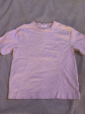 Ljusrosa t-shirt från Gina Tricot - En basic ljusrosa t-shirt från Gina Tricot, basically basics-kollektionen. Klassisk rund halsringning och korta ärmar. Tillverkad i mjuk bomull som känns skön mot huden. Perfekt att styla med jeans eller kjol för en clean look.