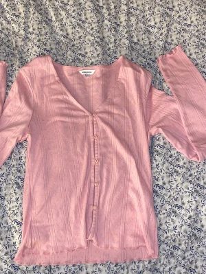 Rosa kofta med knappar från Bubbleroom - Soft pink button-up top from Bubble Room in size XS. Feminine ribbed fabric with delicate pointelle details and cute lettuce-edge hems on the sleeves and bottom. Features a flattering V-neck and buttons down the front. Perfect for a romantic, Y2K or everyday look. In good condition.
