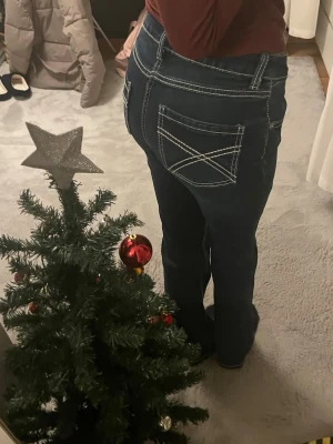 Blå bootcut jeans från Denim Day - Säljer ett par mörkblå jeans från Denim Day i storlek 164. Byxorna har vita kontrastsömmar, klassiska fem fickor och bootcut passform. Materialet är jeans. Snygga detaljer på bakfickorna med korsade sömmar. Passar xs-s