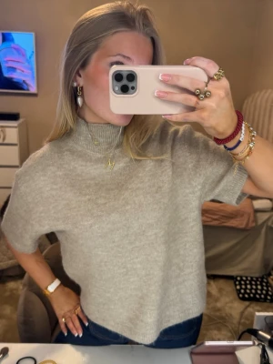 Beige stickad polotröja  - Supermjuk beige stickad polotröja med korta ärmar och relaxed fit. Tröjan har en hög ribbad krage och är gjord i en kashmirblandning som känns lyxig och skön mot huden. Perfekt att styla med jeans eller kjol för en chill men snygg look.