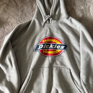 Grå hoodie från Dickies  - Snygg grå hoodie från Dickies med stor färgglad logga på bröstet. Klassisk känguruficka, huva med dragsko och mjukt material. Storlek S. Den är knappt använd och nypris är cirka 700kr. 