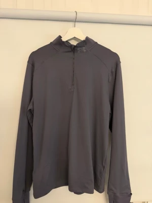 Under Armour träningströja  - Säljer min sambos grå långärmad träningströja från Under Armour med zip. Endast provad en gång då den inte satt bra. 