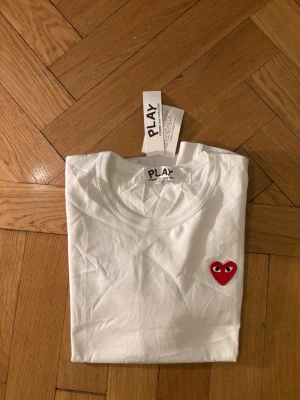 Vit t-shirt Comme des Garçons Play S - Säljer en vit t-shirt från Comme des Garçons Play i storlek S. T shirten är i helt ny och har inga defekter. Hör av vid funderingar!
