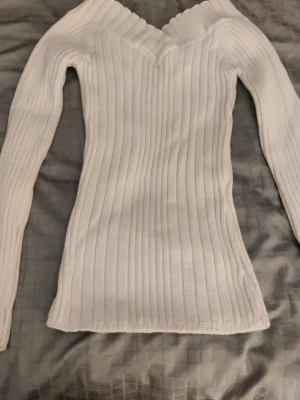 Vit stickad tröja - Snygg vit stickad tröja med ribbad struktur och v-ringad hals. Tröjan har lång ärm och en slim passform som sitter snyggt på kroppen. Märket eller storleken står inte men skulle säga att det är xs eller s