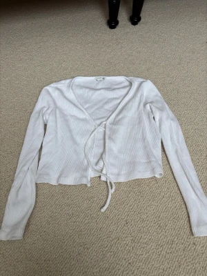 Vit ribbad omlottkofta med knyt - Säljer en vit ribbad omlottkofta från monkl i storlek XXS. Koftan har långa ärmar, v-ringad hals och knyt framtill. Materialet är mjukt och stretchigt, perfekt för lager-på-lager. Enkel och stilren design som passar till många olika looks.
