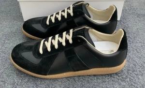 Svarta sneakers Maison Margiela - Maison Margiela sneakers i svart skinn och mocka med beige snörning och gummisula. Klassisk rund tå och platt sula, insida i ljusbeige. Snygg retrostil med kontrasterande material och detaljer. Perfekt för dig som gillar stilrena och tidlösa sneakers.