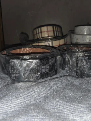 Svart och grå rutig Louis Vuitton bälte - Snygg bälte från Louis Vuitton i svart och grått med rutigt mönster. Västen har en klassisk form och är tillverkad i syntetmaterial med en exklusiv känsla. Perfekt för dig som vill ha en stilren och trendig look med ikonisk LV-detalj framtill.