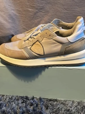 Beige Philippe Model sneakers - Snygga sneakers från Philippe Model i beige och grå toner. Skorna har en rund tå, platt sula och snörning framtill. Materialmix med mocka, mesh och skinn ger en lyxig känsla. Ikonisk skölddetalj på sidan och diskret logga på plösen. Perfekt för dig som gillar stilrena sneakers. Box ingår ej, skriv vid frågor eller funderingar!