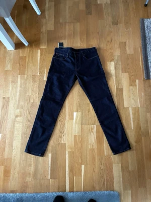 Emporio Armani J06 slim fit jeans blå - Snygga mörkblå jeans från Emporio Armani, modell J06 slim fit med brun snygg broderad detalj på höger ben. Etikett är kvar och de är helt oanvända.