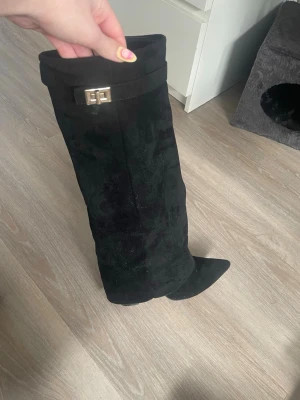 Svarta mockastövlar med spetsig tå - Säljer ett par svarta stövlar i mocka med spetsig tå och snyggt guldfärgat spänne upptill. Stövlarna har en klassisk och stilren look som passar perfekt till höst och vinter. Materialet är mjukt och ger en lyxig känsla.