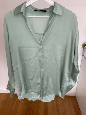 Ljusgrön silkeslen skjorta från Zara - Ljusgrön skjorta från Zara med klassisk krage och knappar framtill. Materialet är silkeslent och har en lätt glansig finish. Skjortan har lång ärm och en lös passform. Stl xs, kan även passa s.